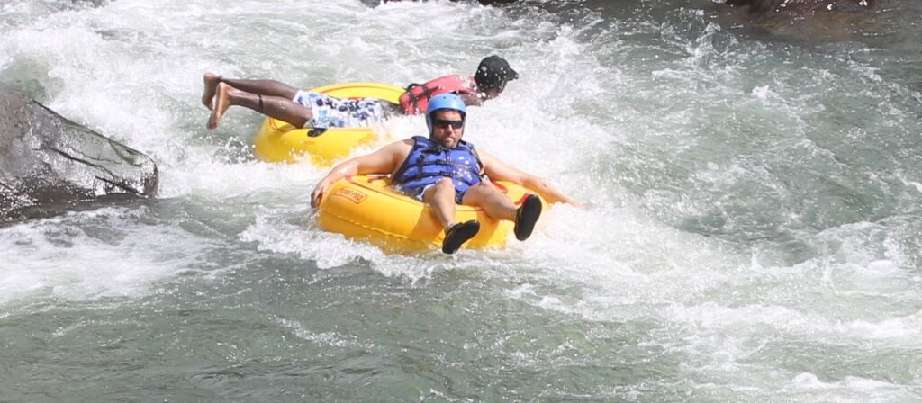River tubing guests navigating gentle rapids with a guide nearby for safety in Dominica